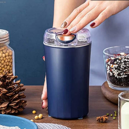 Navy blue spice grinder being used with a hand on a wooden surface.
